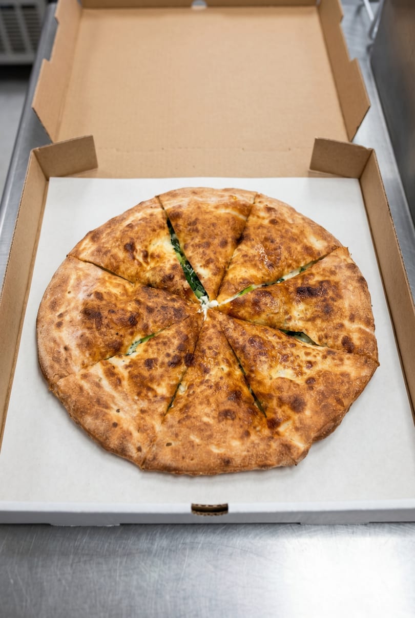 A freshly baked, sliced calzone with a golden-brown crust, filled with spinach and cheese, in a pizza box.